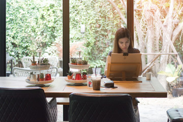 Fototapeta premium Beautiful woman embodying her ideas on paper with help of paintbrush and watercolors, interior of coffee cafe on natural background.