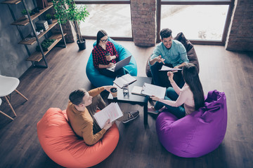 Top above high angle view of nice attractive smart clever interns managers reviewing development attending internship sitting on bag chair at industrial loft interior workplace workstation