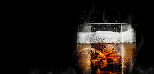 Soft drink glass with ice splash on cool smoke background. Cola glass with summer refreshment. - obrazy, fototapety, plakaty