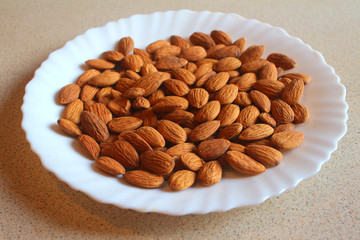 Raw peeled almond grains on a white plate on the table.. Side view