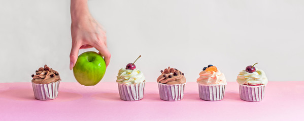 apple among cupcakes, healthy food choices, female hand picks green apple, fatty sweet food, diet,...