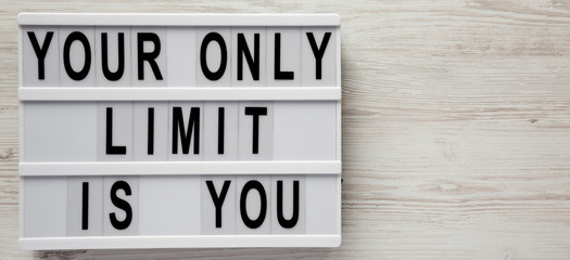 Modern board with 'Your only limit is you' words on a white wooden background, top view. From above, flat lay, overhead. Space for text.