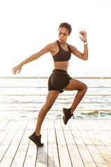 Fototapeta na wymiar Image of athletic young woman in sportive clothes doing workout by seaside in morning