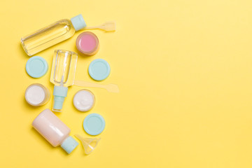 Top view composition of small travelling bottles and jars for cosmetic products on yellow background. Facial skin care concept with copy space for your design