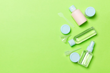 Top view composition of small travelling bottles and jars for cosmetic products on green background. Facial skin care concept with copy space for your design