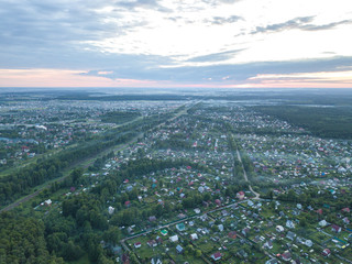Aerial view of the village at summer season. Roofs of the houses and farms with green grass and trees surrounded by forest in evening haze. Moscow region, Russia.