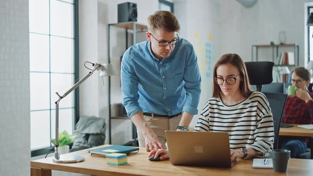 Young Casual Business Couple are Using Laptop in Creative Agency Loft. Friendly Easygoing Coworking Atmosphere. They Discuss and Brainstorm Ideas. Manager Explaining New Work Strategy.