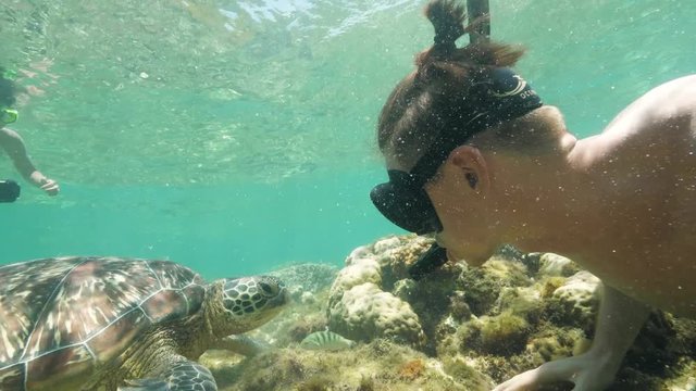 Young man shooting selfie video with sea turtle while snorkeling with mask and tube. Young woman making underwater photo to man and turtle while snorkeling in sea.