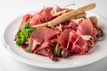 Slicing gourmet meat, prosciutto from beef and pork with berries, cheese, vegetables. Banquet festive dishes. Gourmet restaurant menu. White background.