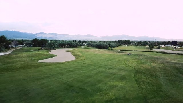 Drone Shot flying over a fairway on a luxury green golf course. A golf cart can be seen driving across the fairway.