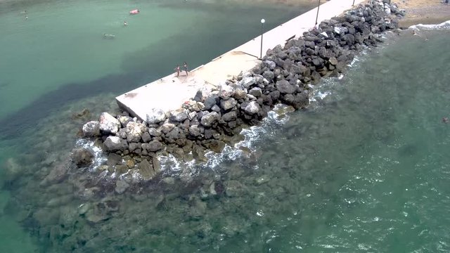 Aerial view of stunning turquoise sea in the summer with pier and rocks that water pops up on them in the area of Agia Paraskevi Halkidiki, Greece, circular movement by drone