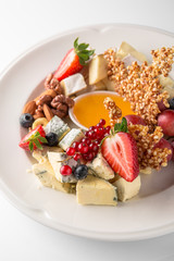 Luxurious cheese plate of different types of cheese: camembert, dorblu, parmesan, cheddar, with honey, caramel, berries. Banquet festive dishes. Gourmet restaurant menu. White background.