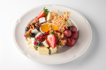 Luxurious cheese plate of different types of cheese: camembert, dorblu, parmesan, cheddar, with honey, caramel, berries. Banquet festive dishes. Gourmet restaurant menu. White background.
