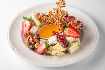 Luxurious cheese plate of different types of cheese: camembert, dorblu, parmesan, cheddar, with honey, caramel, berries. Banquet festive dishes. Gourmet restaurant menu. White background.