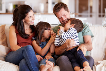 Mid adult white couple and their two young children sitting on a sofa at home smiling at each other