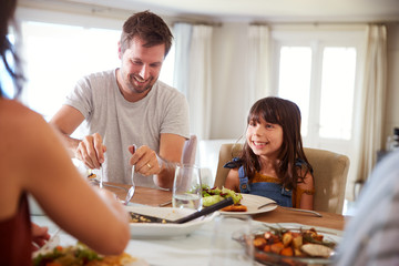 Young girl waiting for her dad to serve food at the dinner table during a family meal, close up