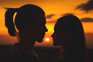 Close-up of the silhouettes of a young millenial couple in love with a man and girl against the sunset golden sky. They look at each other. Young family
