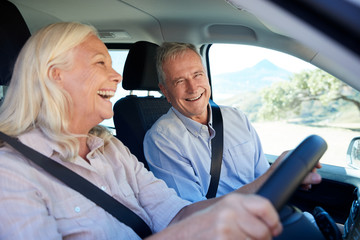 Senior white woman and her husband driving in their car laughing together, close up, side view