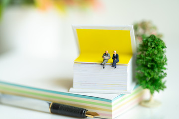 Miniature people: Business team sitting on book, reading news paper with copy space using as background business, education concept.
