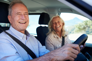 Happy senior white couple driving in their car, smiling to camera, side view, close up