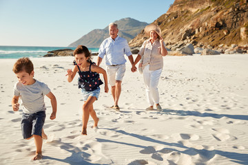 Senior white couple and their grandchildren walking on a sunny beach, close up