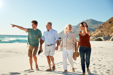 Mid adult and senior white couples walking on a beach together talking, full length, close up
