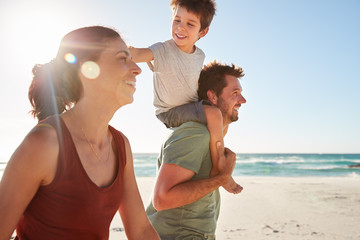 Mid adult white couple walking on a beach, dad carrying son on his shoulders, close up, lens flare