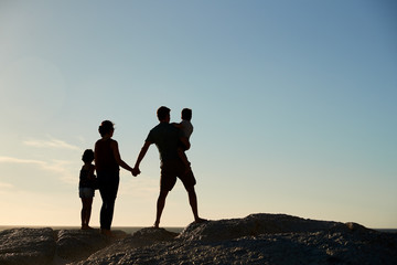 Mid adult parents and two pre-teen children standing on beach admiring view, full length, silhouette