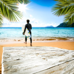 Table background and the wooden board and surfier with surfing board in the beautiful ocean and sunny beach view