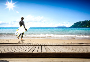 Table background and the wooden board and surfier with surfing board in the beautiful ocean and sunny beach view