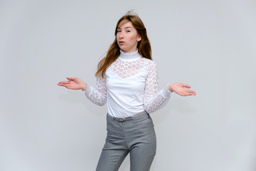 Portrait of a knee-high young pretty brunette girl woman with beautiful long hair on a white background in a white jacket and gray pants. He talks, shows his hands with emotions in various poses.