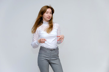 Portrait of a knee-high young pretty brunette girl woman with beautiful long hair on a white background in a white jacket and gray pants. He talks, shows his hands with emotions in various poses.