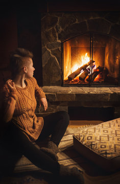 Hipster girl sitting near fireplace in cozy evening atmosphere