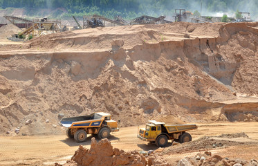 Big yellow dump trucks working in the open-pit. Transporting sand and minerals. Mining quarry for the production of crushed stone, sand and gravel for use in the construction industry - image