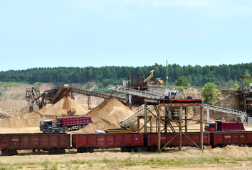 View on the mining quarry. Plant for the production sand and gravel for the construction industry. Mechanical machine, conveyor belt for crushing stone. Dump trucks transporting sand in the open-pit.