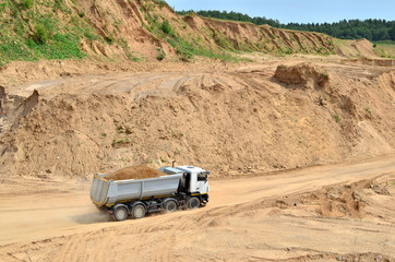 Big yellow dump truck transporting sand in an open-pit mining quarry. Mining quarry for the production of crushed stone, sand and gravel for use in the construction industry - image