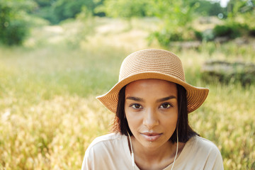 Portrait of beautiful woman wearing straw hat using earphones while sitting on grass in green park