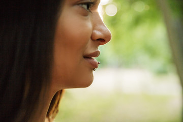 Cropped portrait in profile of young woman wearing lip piercing walking in green park