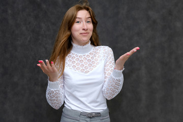 Portrait to the waist of a young pretty brunette girl woman with beautiful long hair on a gray background in a white jacket. He talks, smiles, shows his hands with emotions in various poses.