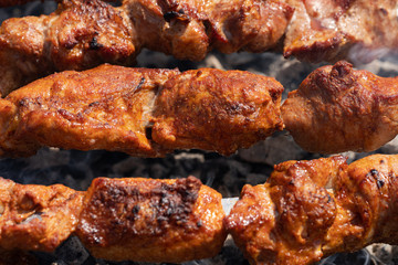 Grilled tasty juicy pork shish kebab cooking on metal skewers on charcoal grill with fragrant fire smoke. Close-up view, selective focus on pieces of delicious roast meat. Cooking summer picnic.