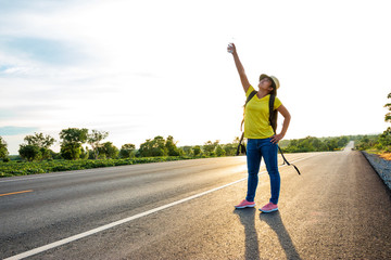 Women tourists carrying a backpack that holds his hands up to the sky on the highway with the golden light of the sun, Happy mood from tourism.