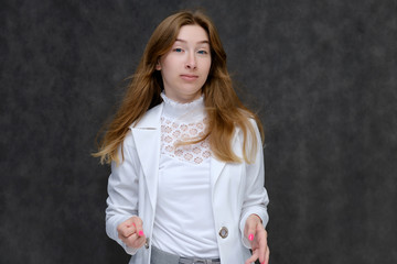 Portrait to the waist of a young pretty brunette girl woman with beautiful long hair on a gray background in a white jacket. He talks, smiles, shows his hands with emotions in various poses.