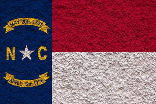 The national flag of the US state North Carolina in against a gray wall stony surface on the day of independence in blue red and white. Political and religious disputes, customs and delivery.