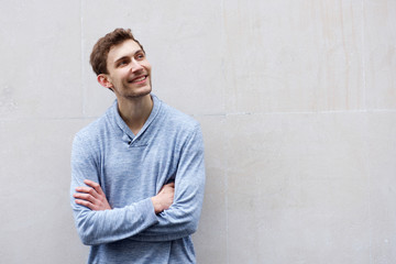 young man smiling by wall with arms crossed and looking away