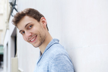 Close up side of young man leaning against wall and smiling