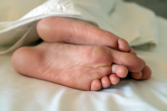 Men's feet under a white blanket. Sleeping man under a white blanket.