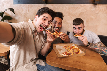 Three cheerful men eating pizza at the cafe table