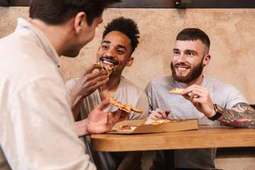 Three cheerful men eating pizza at the cafe table