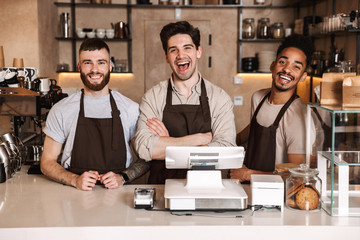 Group of cheerful men baristas wearing aprons