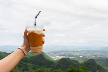 closeup of woman's hand show cup of espresso iced coffee with mountain view. soft-focus and over light in the background